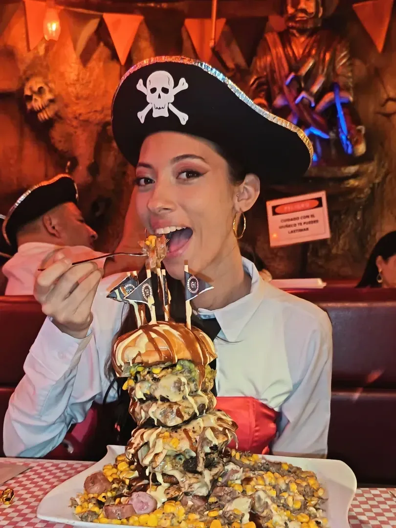 Clienta con sombrero pirata disfrutando de una montaña de papas con carnes en La Cueva del Pirata